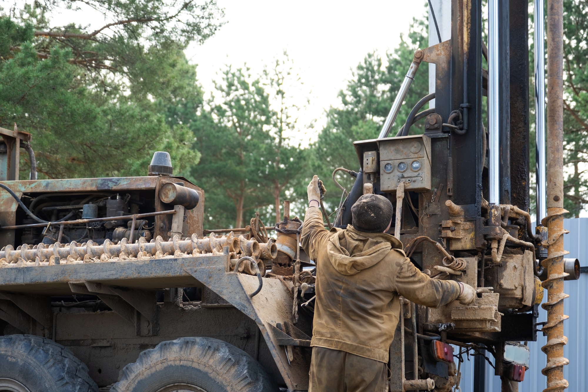 Team of workers with drilling rig on car are drilling artesian well for water in ground